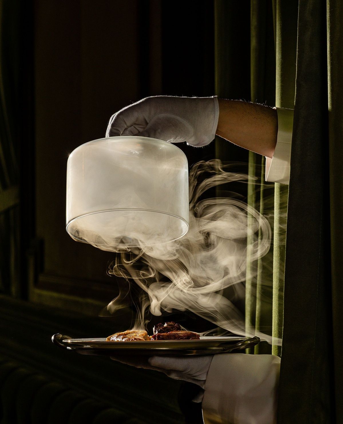 White-gloved waiter lifting a smoke-filled cloche over a fine dining dish